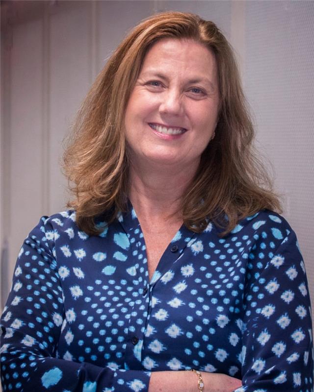 Jenni Evans smiles for a photo in a blue polka-dotted blouse.
